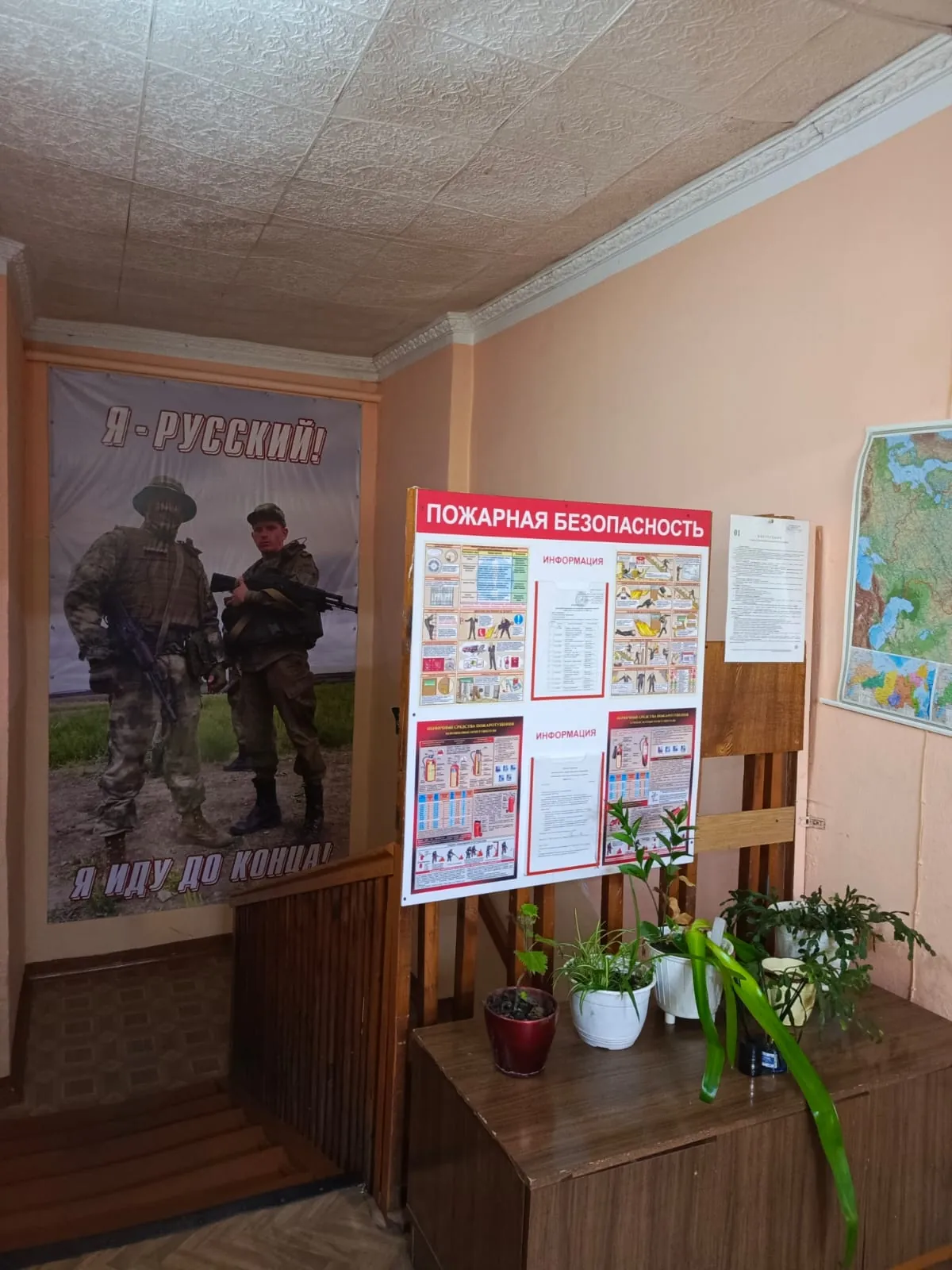 Холл с плакатом, стендом по пожарной безопасности и цветами у лестницы