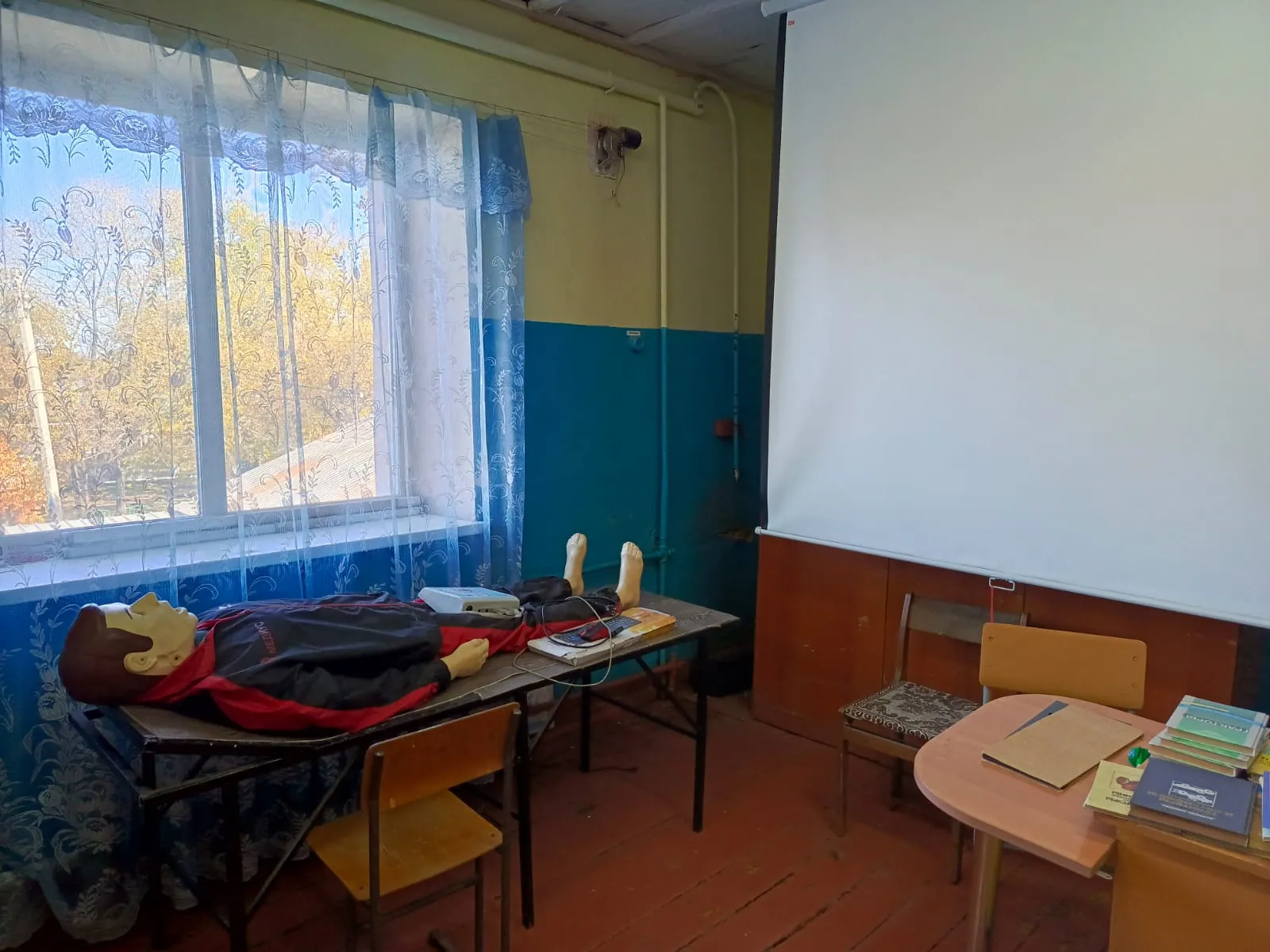 Манекен для отработки первой помощи на столе у окна, экран проектора