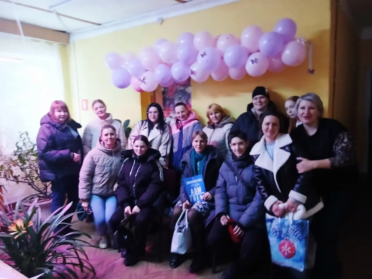 Группа женщин в зимней одежде на фоне сиреневых шаров